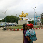 Woman with child passes a gold statue of Aung San, Myanmar