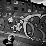 A boy covers his face while walking along the wall full of graffiti