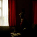 Member of Sisters of Mercy convent stands in the shadow beside the window, view from the inside