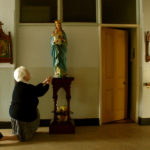 Sister kneels in front of the Virgin Mary statue