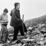 Barefoot woman with a rosary in her hands and a man with a stick and rosary walk the rocky path at Croagh Patrick pilgrimage