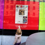 Girl points with her finger at a poster looks like The Irish Times front-page
