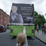 Girl points with her finger at the back of the bus with pro LGBT poster