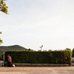 A lonely woman kneels next to the hedge in Medjugorje with crowds in the background