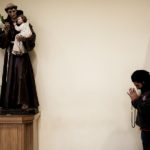 A man prays kneeling in front of the statue of a saint