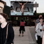 People walk near the giant screen displaying Christ on the cross