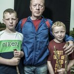 Man with 2 boys on his sides - all with walking sticks - Croagh Patrick pilgrims portrait with partially black background