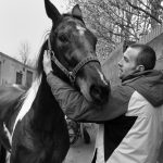 Young man stands in a back alley touching the horse's neck