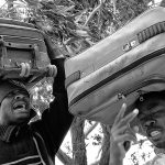 2 African refugees holds their suitcases on their heads, Choucha camp
