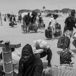 Refugees with suitcases walking into Choucha camp in the heavy desert wind
