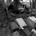 5 tombstones lay on the ground while a group of 5 men dig out with the shovels